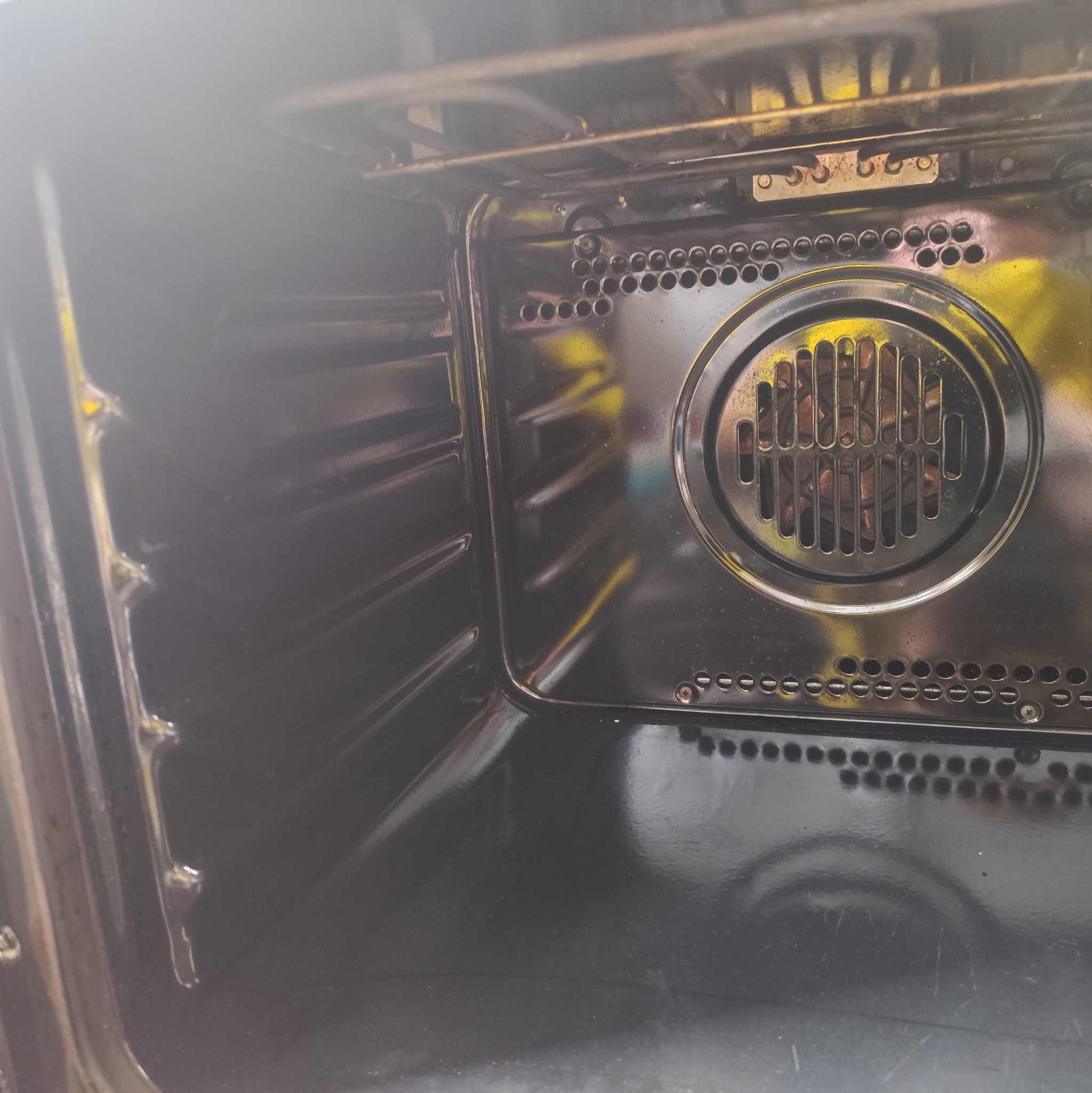 Wnętrze czarnego piekarnika po czyszczeniu, widoczne metalowe elementy grzewcze i boczne prowadnice. Wnętrze jest czyste i błyszczące.