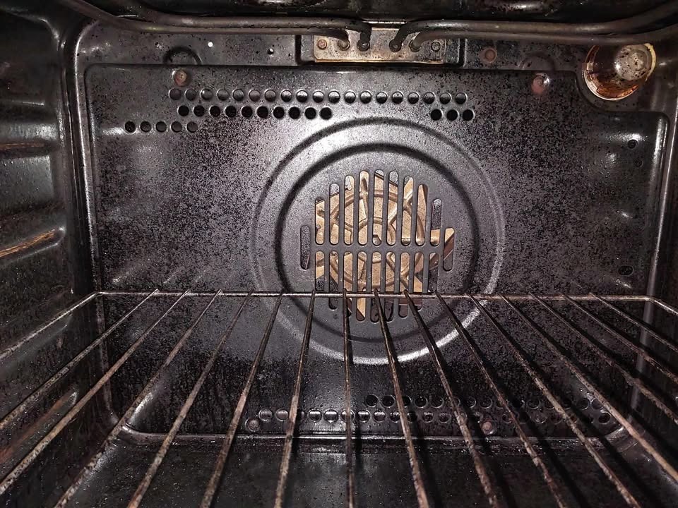 Wnętrze brudnego piekarnika z rusztem, widoczne przypalone resztki jedzenia na ściankach i grzałce. Metalowe elementy pokryte tłustym osadem.