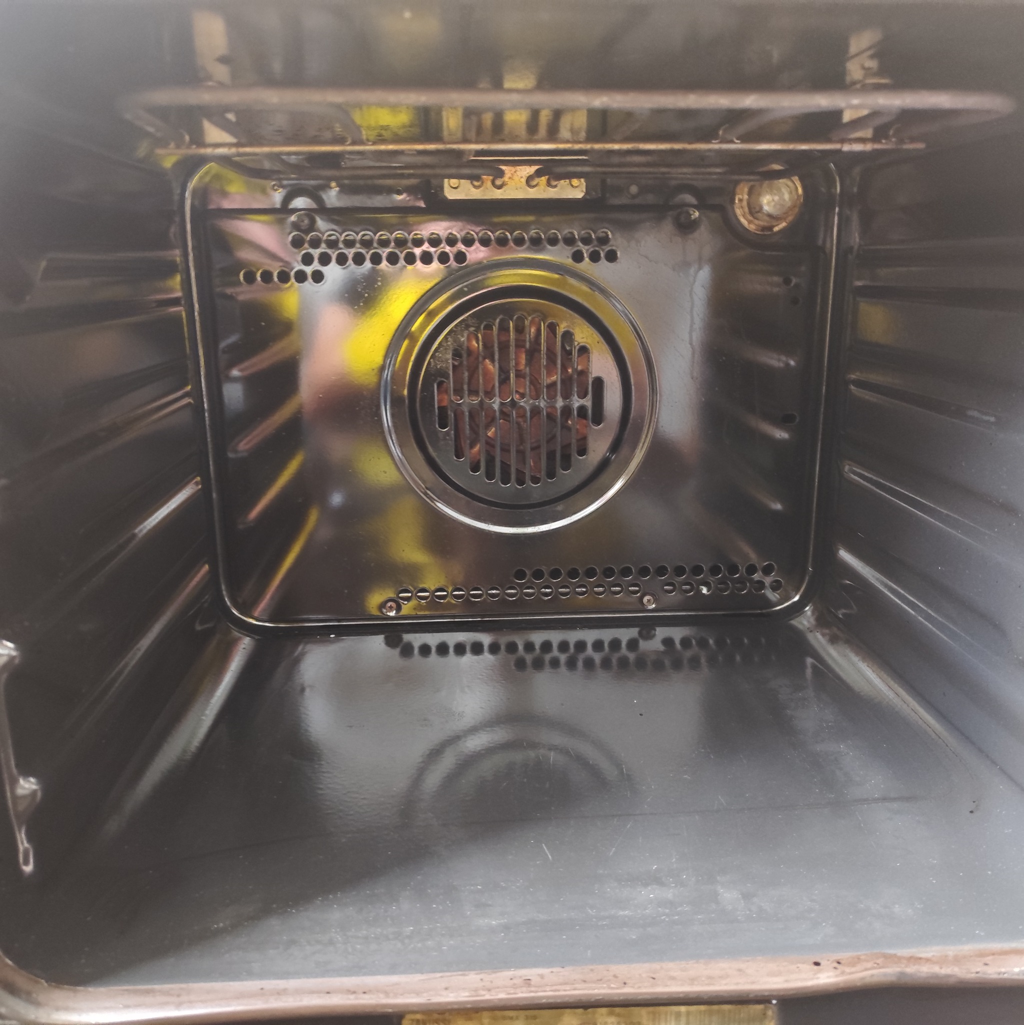 Wnętrze piekarnika z widoczną grzałką i otworami wentylacyjnymi. Metalowe elementy odbijają światło, ukazując czystą powierzchnię po sprzątaniu.