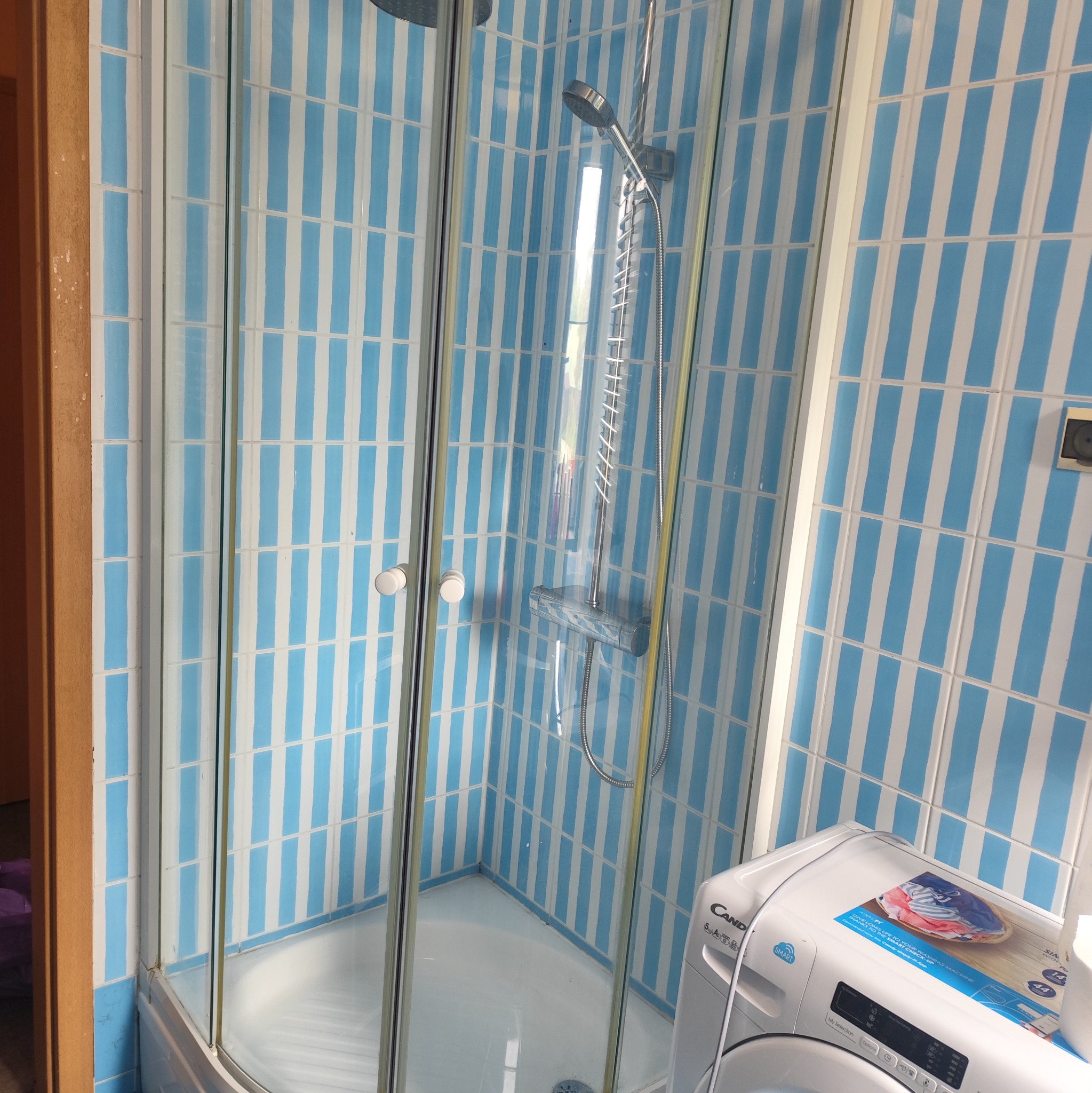 Kabina prysznicowa z niebiesko-białymi płytkami w pionowe pasy, widoczna pralka. Czysta, gotowa do użytku łazienka po sprzątaniu.