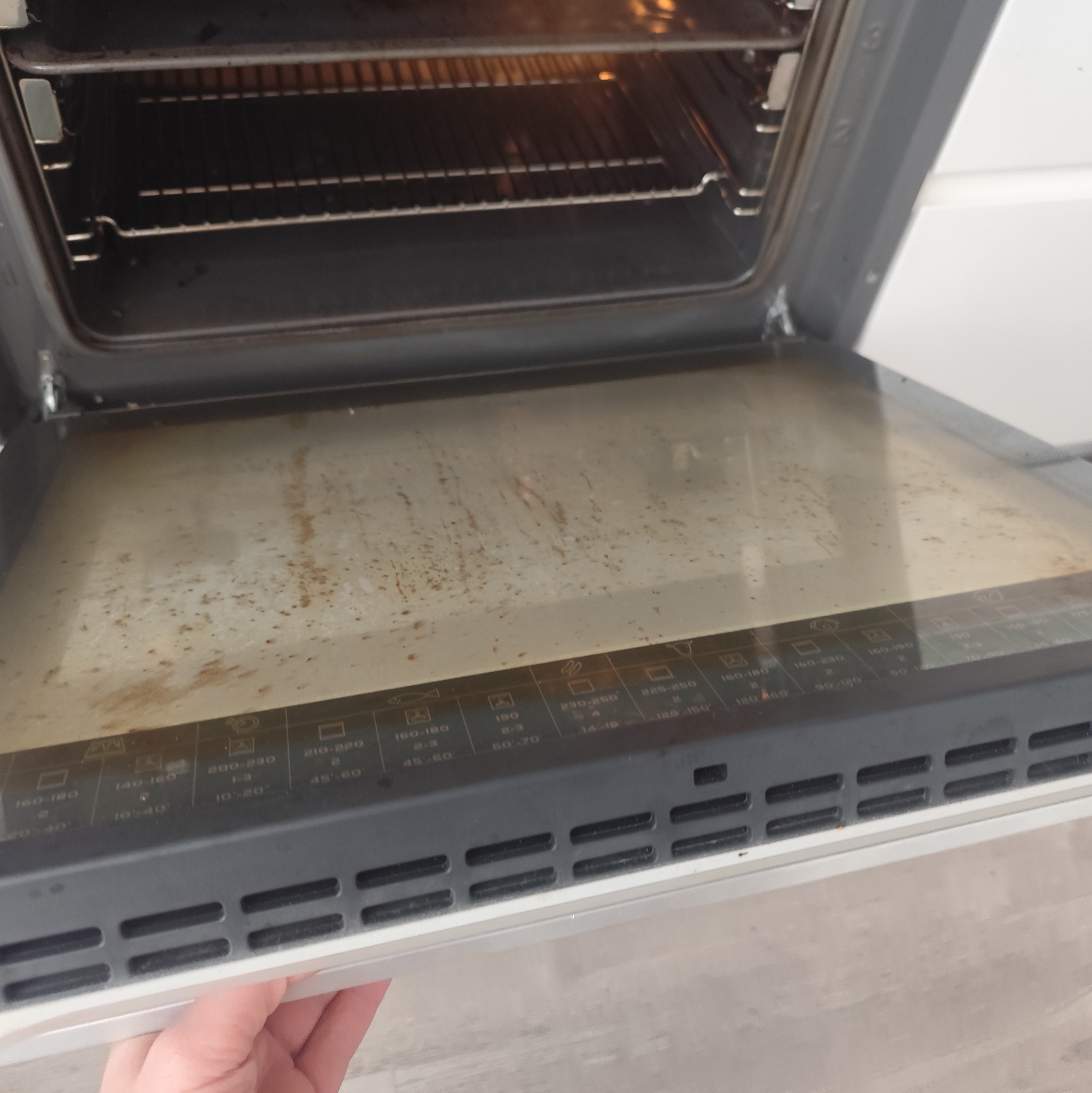 Brudny piekarnik z otwartymi drzwiczkami, widoczne resztki jedzenia na szybie i wewnątrz. Potrzeba gruntownego czyszczenia wnętrza piekarnika.