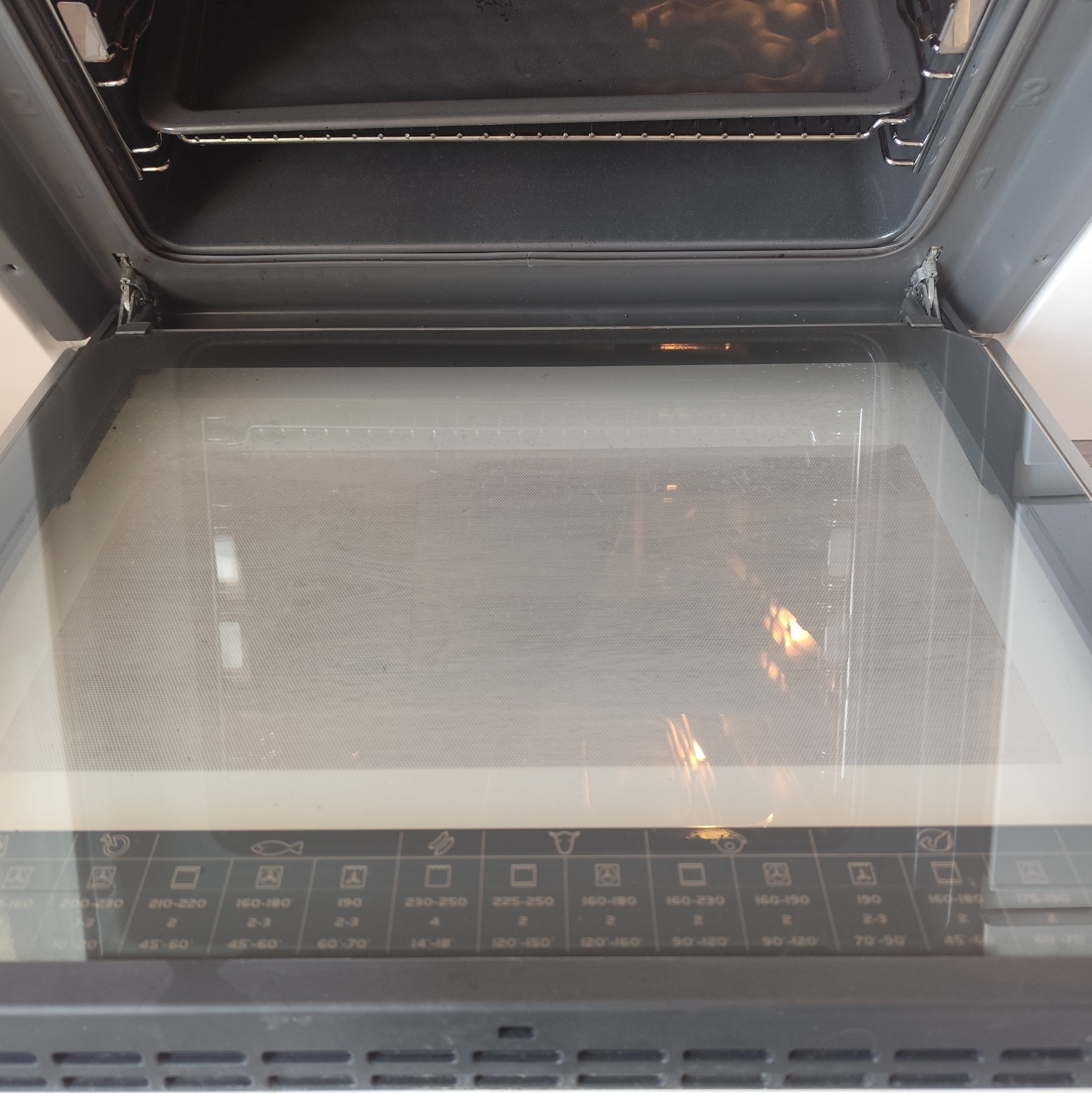 Otwarty piekarnik elektryczny z widocznymi zabrudzeniami na szklanych drzwiach i wewnątrz, co sugeruje potrzebę czyszczenia. Widoczne pokrętła i oznaczenia funkcji.