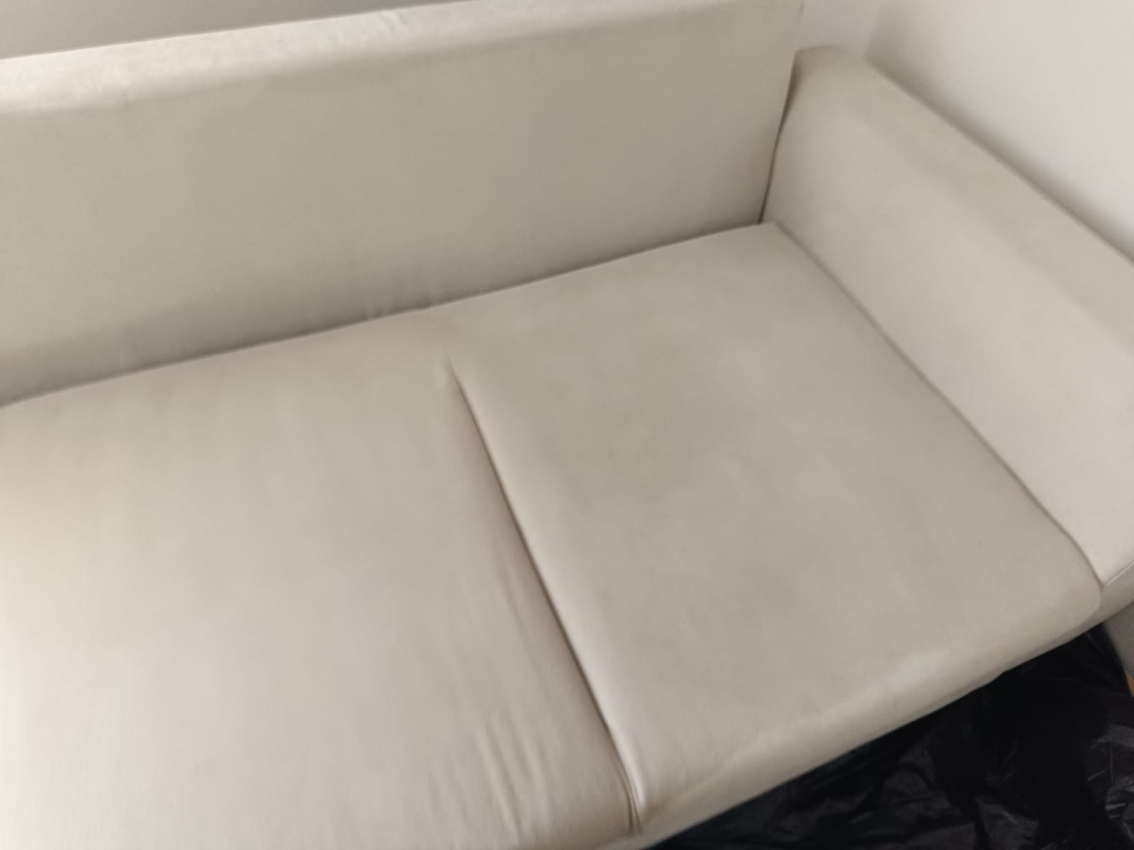 Jasna, tapicerowana sofa z widocznym efektem czyszczenia. Dwie różne faktury na siedzisku sugerują rezultat prania tapicerki. Minimalistyczne tło.