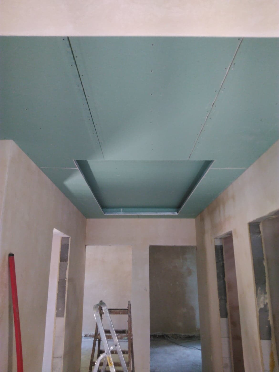 Montaż sufitu podwieszanego z płyt gipsowo-kartonowych z wnęką, widoczna drabina i poziomica, ściany przygotowane do dalszych prac wykończeniowych.