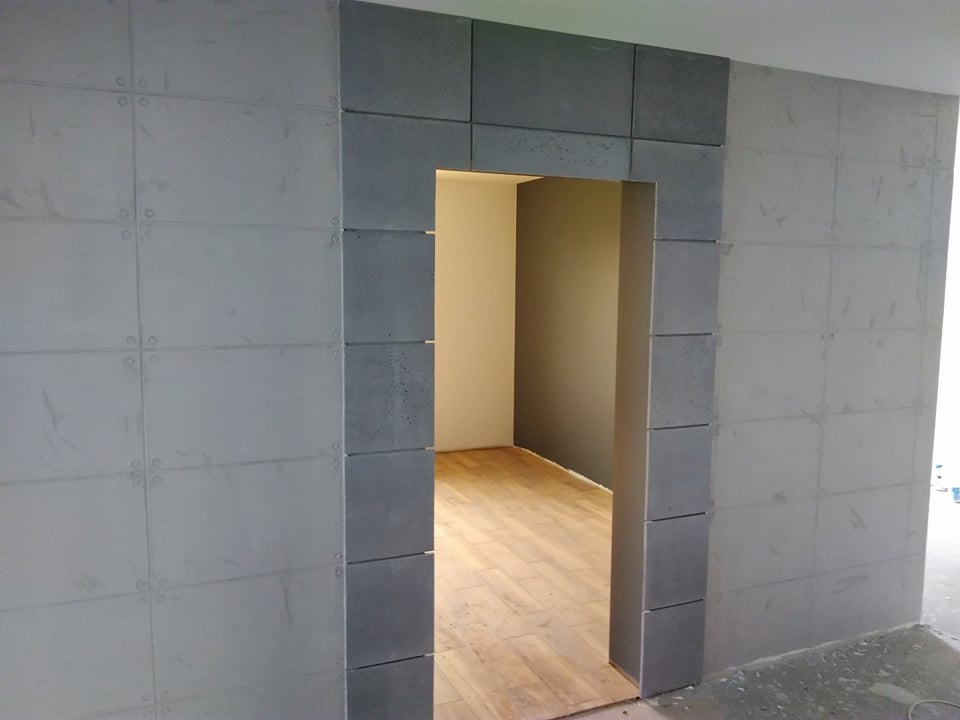 Wykończone wejście do pokoju z szarymi, betonowymi płytami imitującymi cegły na ścianie i ościeżnicy, widoczna podłoga z paneli.