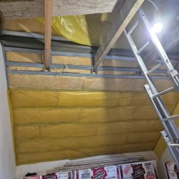 G-N.gut - Ocieplenie poddasza wełną mineralną, widoczne metalowe profile, folia paroizolacyjna i opakowania styropianu. Prace wykończeniowe na poddaszu.