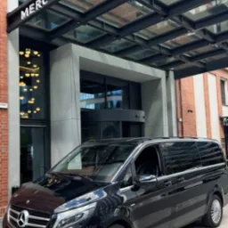 Czarny van Mercedes-Benz V-klasy zaparkowany przed hotelem Mercure, sugerujący luksusowy transport osób. Widoczne logo firmy transportowej.