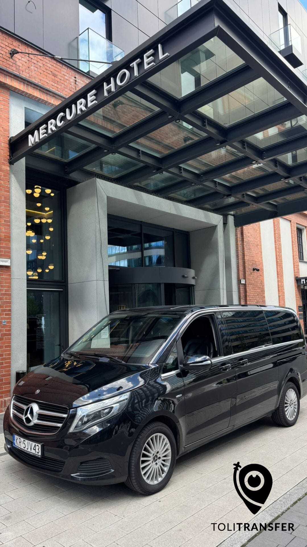 Czarny van Mercedes-Benz V-klasy zaparkowany przed hotelem Mercure, sugerujący luksusowy transport osób. Widoczne logo firmy transportowej.