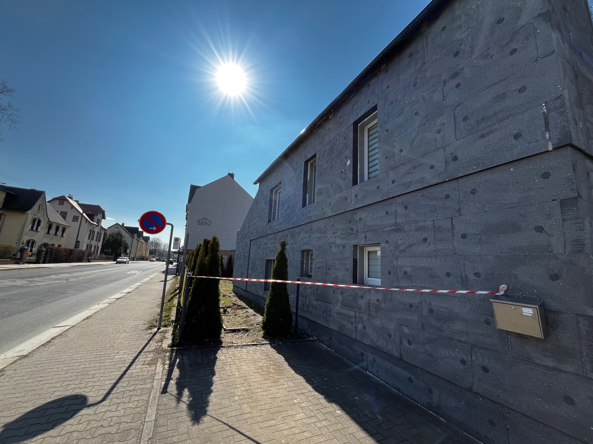 Budynek w trakcie ocieplania elewacji, zabezpieczony taśmą ostrzegawczą, widok z chodnika w słoneczny dzień.