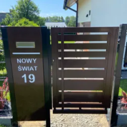 Nowoczesna, brązowa furtka z poziomymi szczeblami i skrzynką na listy z adresem 'Nowy Świat 19', zamontowana przy ogrodzeniu panelowym.