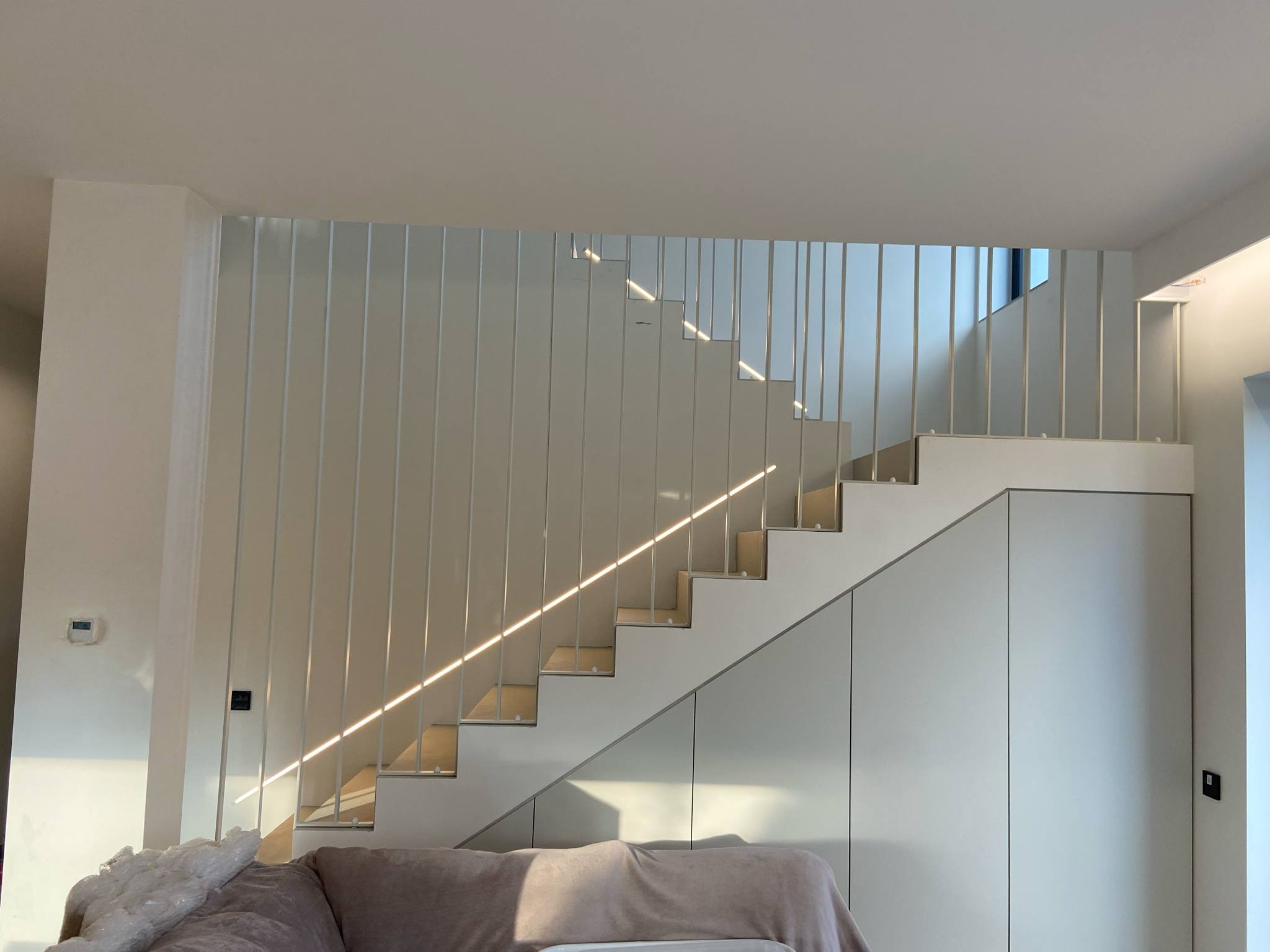 Minimalistyczne, białe schody z pionowymi barierkami, oświetlone promieniami słońca. Nowoczesne rozwiązanie architektoniczne z szafkami pod schodami.