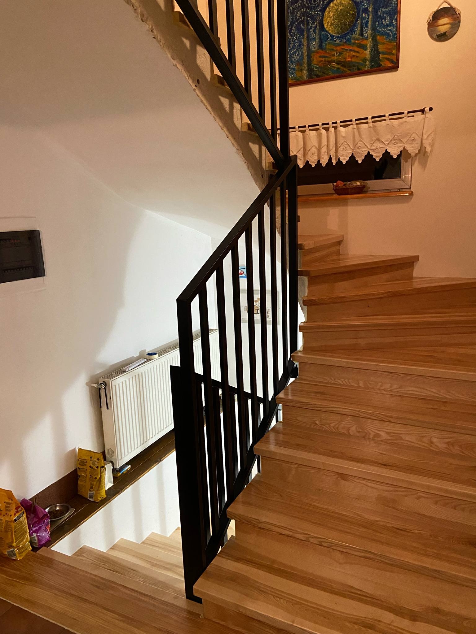 Drewniane schody z czarną, metalową balustradą w jasnym wnętrzu domu. Widok z dołu, podkreślający naturalne wykończenie drewna i nowoczesny design balustrady.