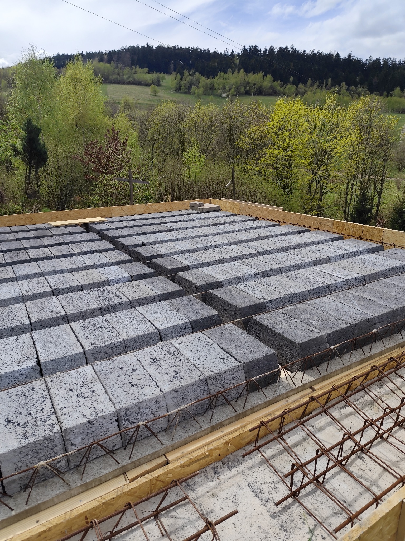 Wypełnienie stropu Teriva bloczkami betonowymi, widoczne zbrojenie i drewniane szalunki, w tle zieleń drzew i błękitne niebo.