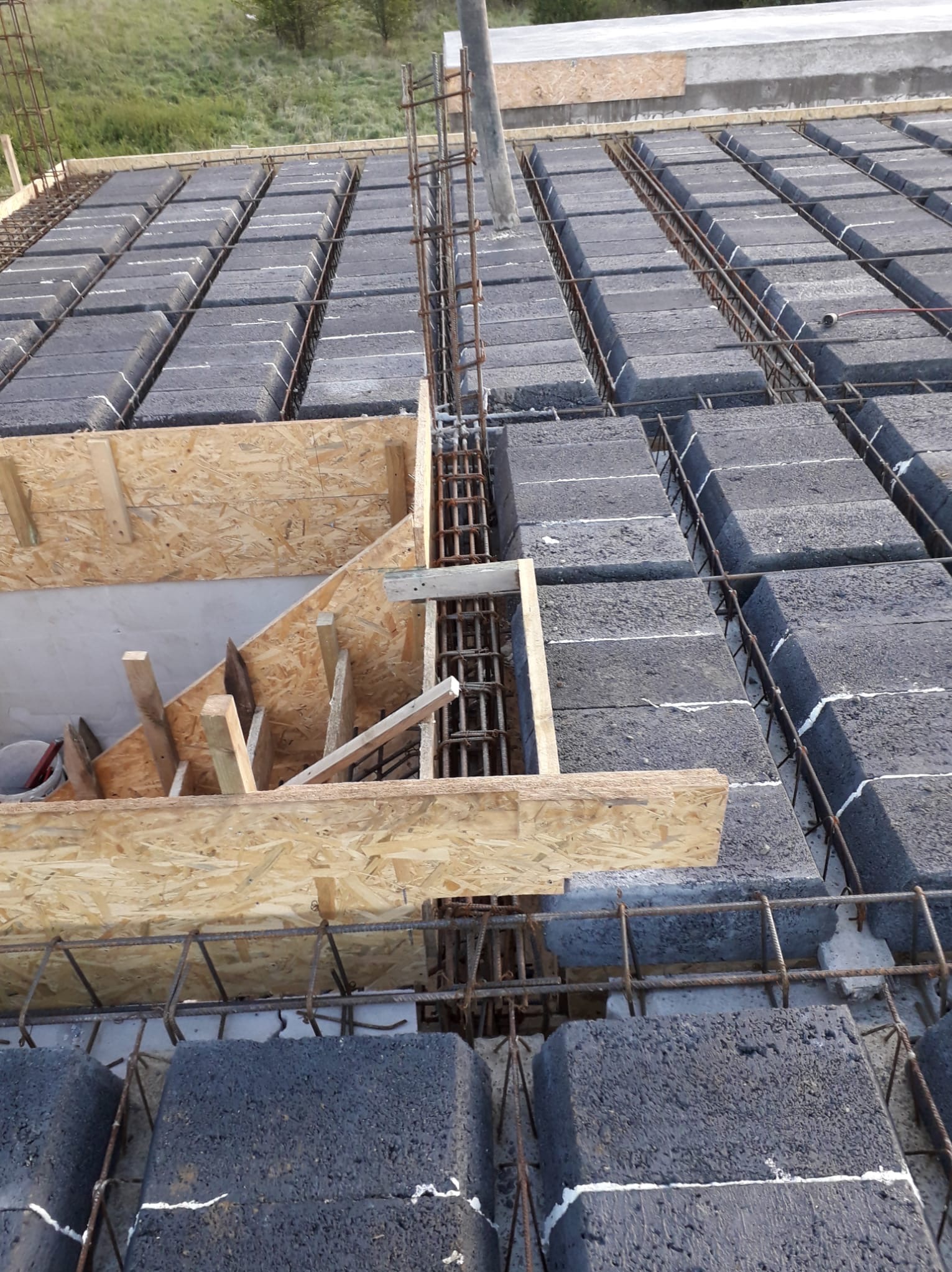 Budowa stropu Teriva: szare pustaki, zbrojenie stalowe i drewniane szalunki w trakcie montażu. Widok z góry na plac budowy.