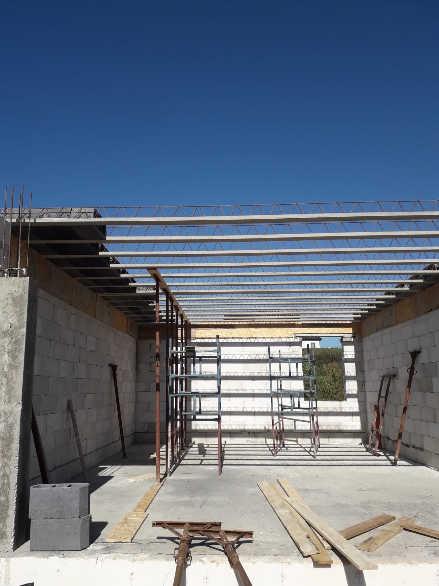 Budowa domu: ściany z betonu komórkowego, strop Teriva z żelbetowymi belkami, rusztowanie. Widok na błękitne niebo. Etap prac murarskich.