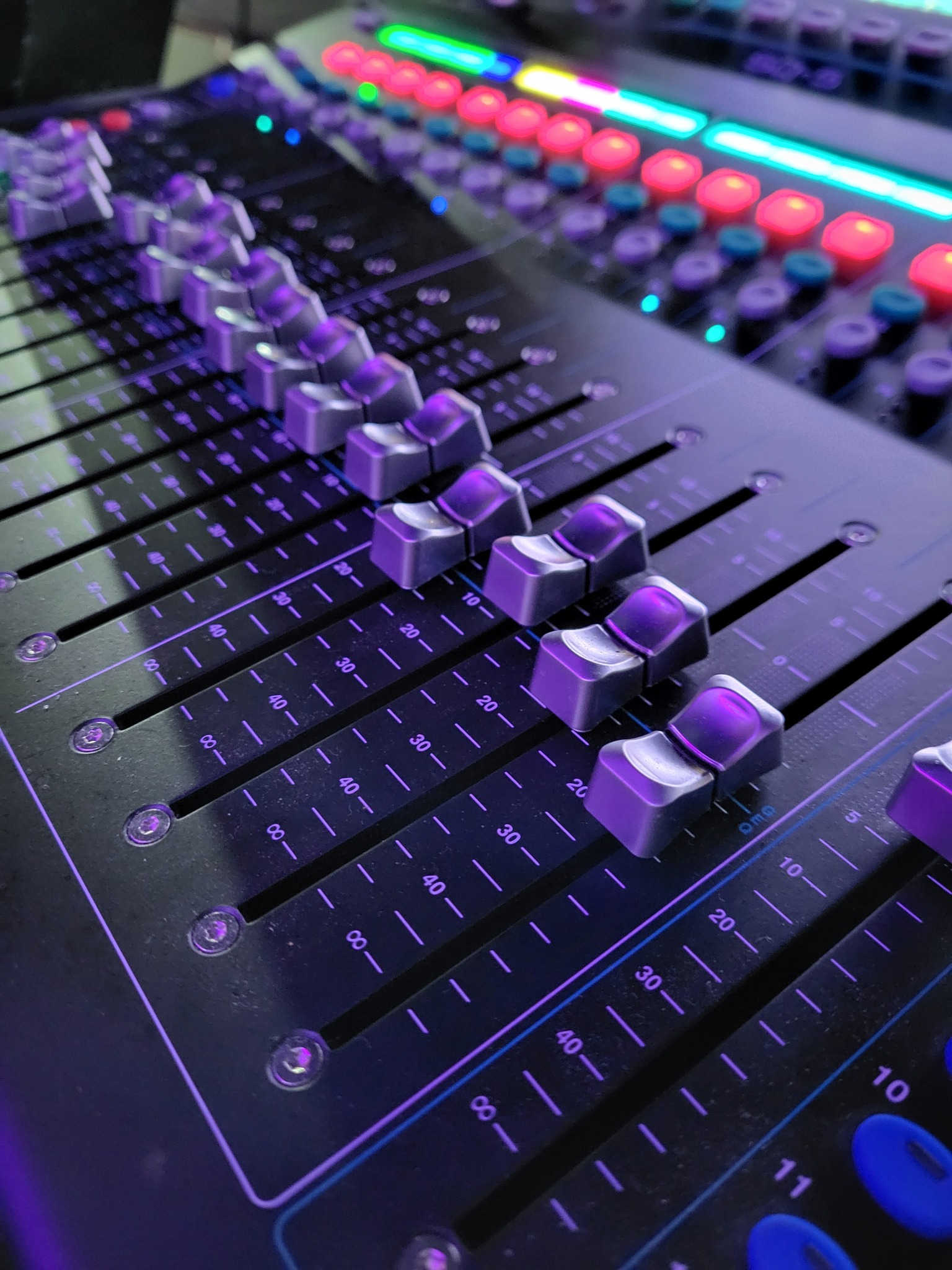Detail of a digital audio mixer with faders and illuminated buttons, angled perspective, showcasing studio equipment for sound engineering or live performance.