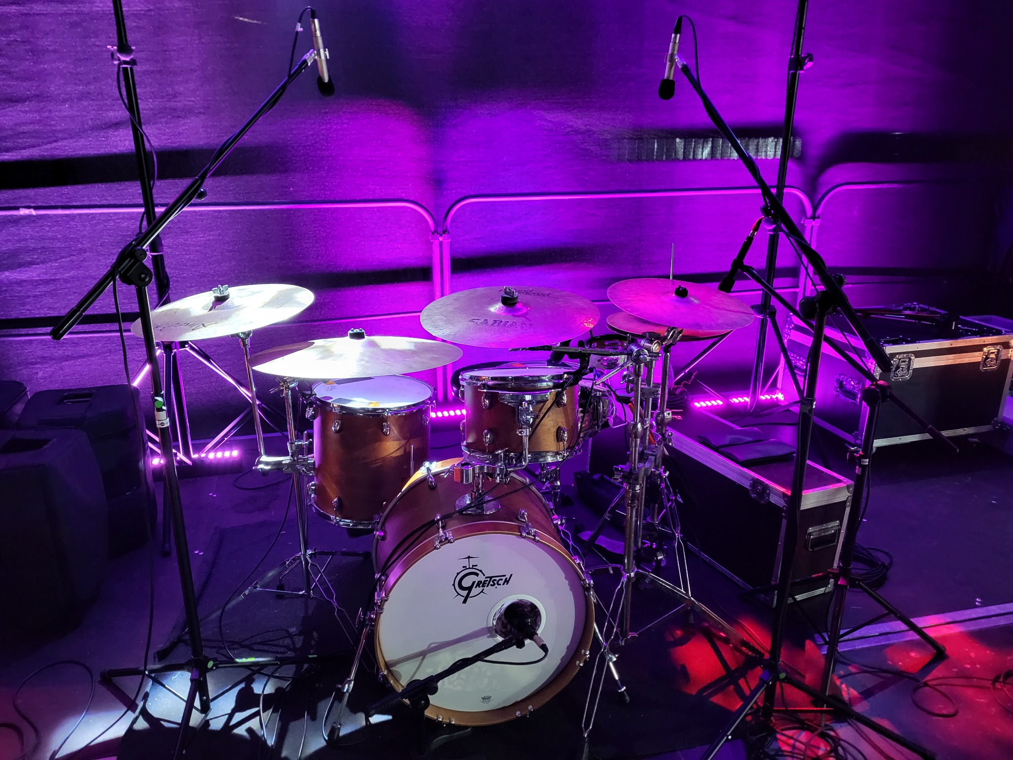 Zestaw perkusyjny Gretsch z talerzami Sabian, mikrofonami i nagłośnieniem, oświetlony fioletowym światłem scenicznym, gotowy do występu na żywo.