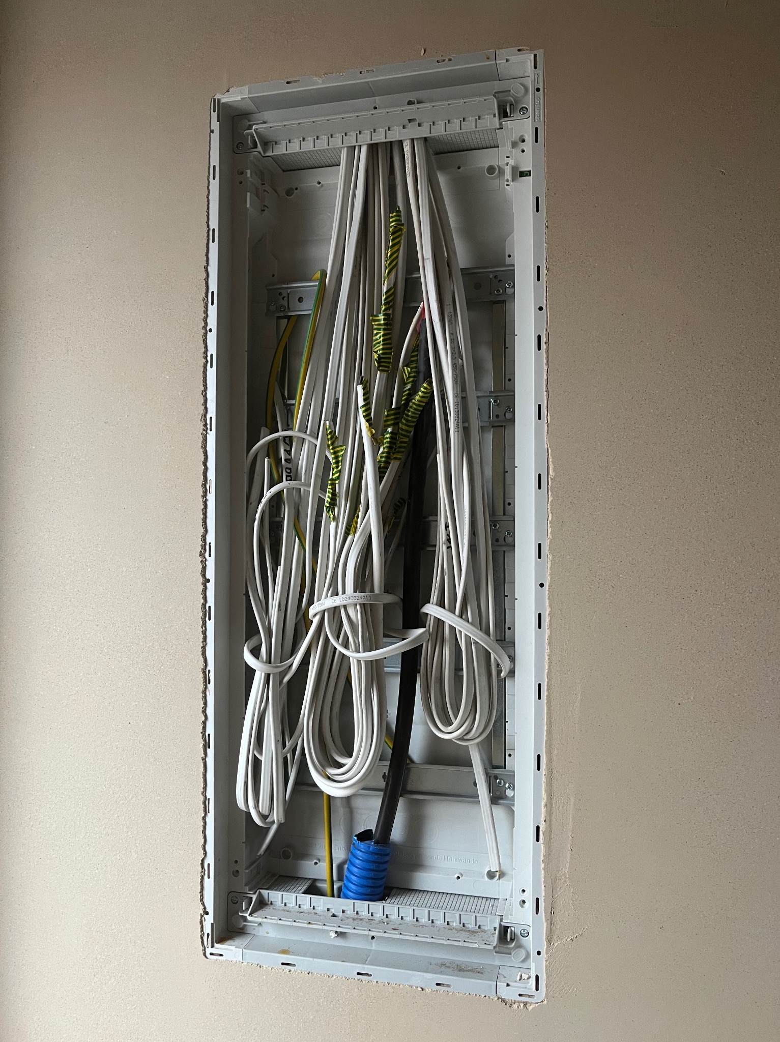 Wewnętrzna instalacja elektryczna w ścianie, widoczne kable w białej skrzynce, przygotowane do podłączenia, ściana pokryta świeżym tynkiem.