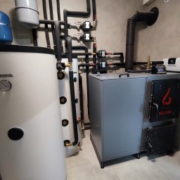 Mateusz Radomski - Szary piec na paliwo stałe marki Syska Welding z czarnym kominem, zbiorniki Kospel i instalacja CO w kotłowni wykończonej beżowymi płytkami.