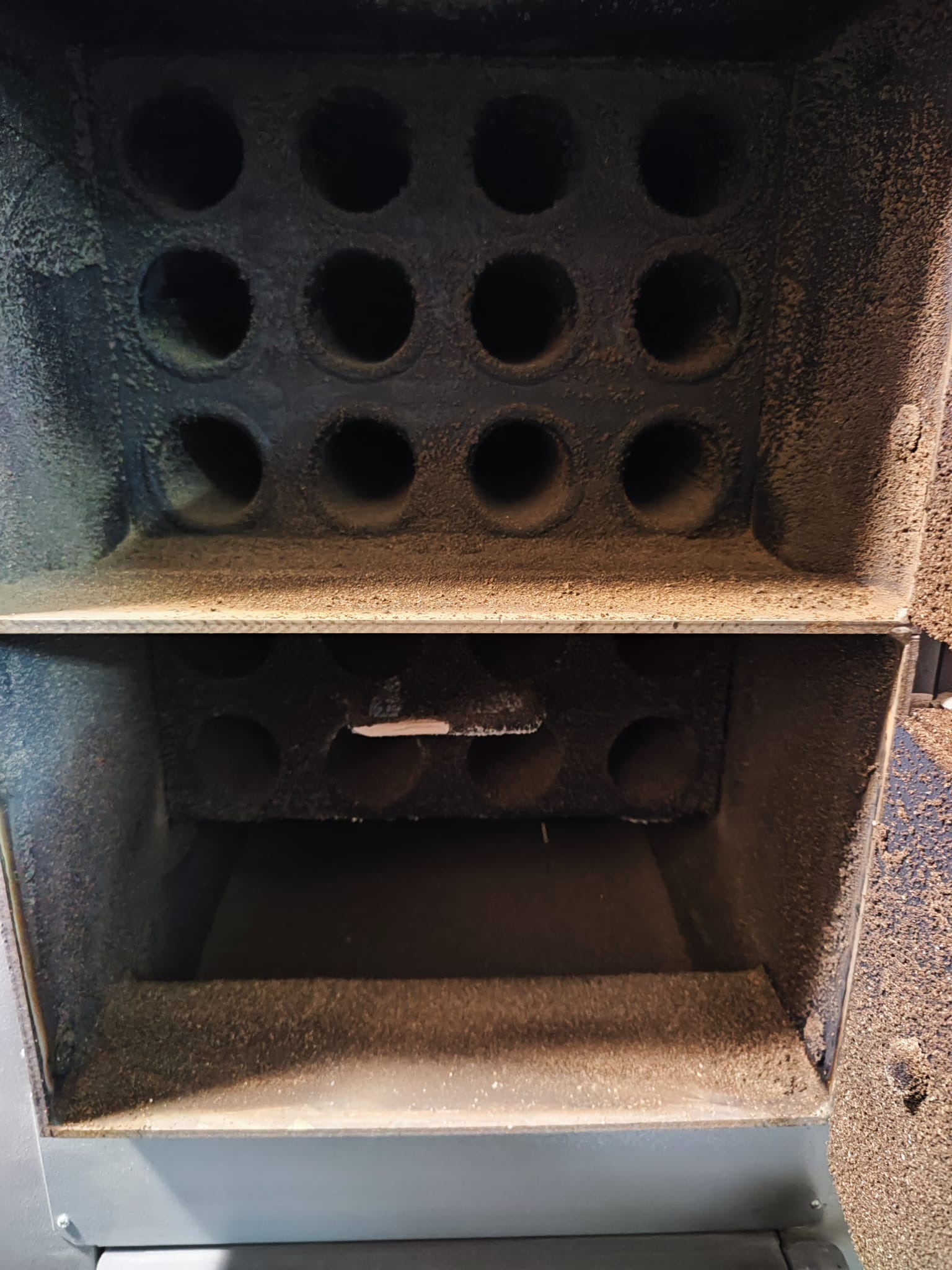 Wnętrze pieca na paliwo stałe z widocznymi otworami i osadem, ukazujące jego konstrukcję i stan użytkowania. Detal paleniska z bliska.