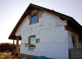 Dom w trakcie ocieplania, z widocznym styropianem na elewacji i oknami. Częściowo ocieplona ściana szczytowa, widoczne niedociągnięcia w obróbce okien.