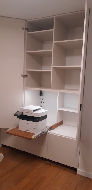 Biała szafa wnękowa z otwartymi drzwiami, półkami i wysuwanym blatem. Na blacie stoi biała drukarka. Oświetlenie LED wewnątrz szafy.