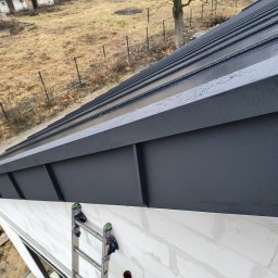 Dach-Expert Igor Smirnow - Nowe, grafitowe pokrycie dachowe z blachy na budynku w Żyrardowie, widok z góry. Na ścianie oparta drabina. Widoczne krople wody na powierzchni.