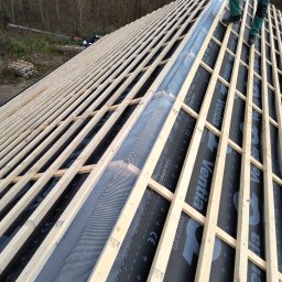 Dach-Expert Igor Smirnow - Konstrukcja dachu w trakcie budowy: drewniane łaty, membrana dachowa z nadrukiem 'Ventia Premium', widoczny fragment orynnowania i osoba w zielonych spodniach.