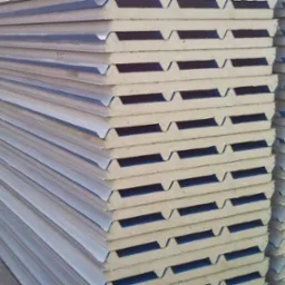 Stos płyt warstwowych z rdzeniem z pianki poliuretanowej i blachą trapezową, ułożonych równo na betonowym podłożu, widoczne detale łączeń i faktura materiałów.