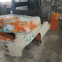 FHU MOBILTECHNIK TOMASZ KUBICA - Wózek widłowy w trakcie renowacji: karoseria z nałożoną szpachlą, częściowo pomalowana na biało, widoczna kabina operatora. Prace blacharskie w warsztacie.