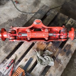 FHU MOBILTECHNIK TOMASZ KUBICA - Czerwony, odnowiony element hydrauliczny wózka widłowego na drewnianej palecie, obok narzędzia i szmatka. Widok z góry, warsztatowy klimat.