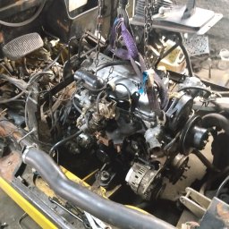 FHU MOBILTECHNIK TOMASZ KUBICA - Silnik wózka widłowego zawieszony na łańcuchach podczas naprawy. Widoczne narzędzia i elementy konstrukcyjne pojazdu. Żółta rama wózka.