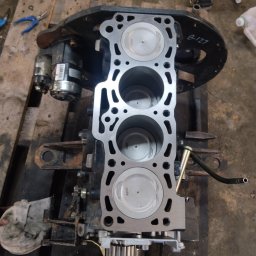 FHU MOBILTECHNIK TOMASZ KUBICA - Silnik spalinowy z trzema cylindrami i tłokami, widoczny na drewnianej palecie. Elementy silnika są czyste, co sugeruje niedawny serwis lub naprawę.