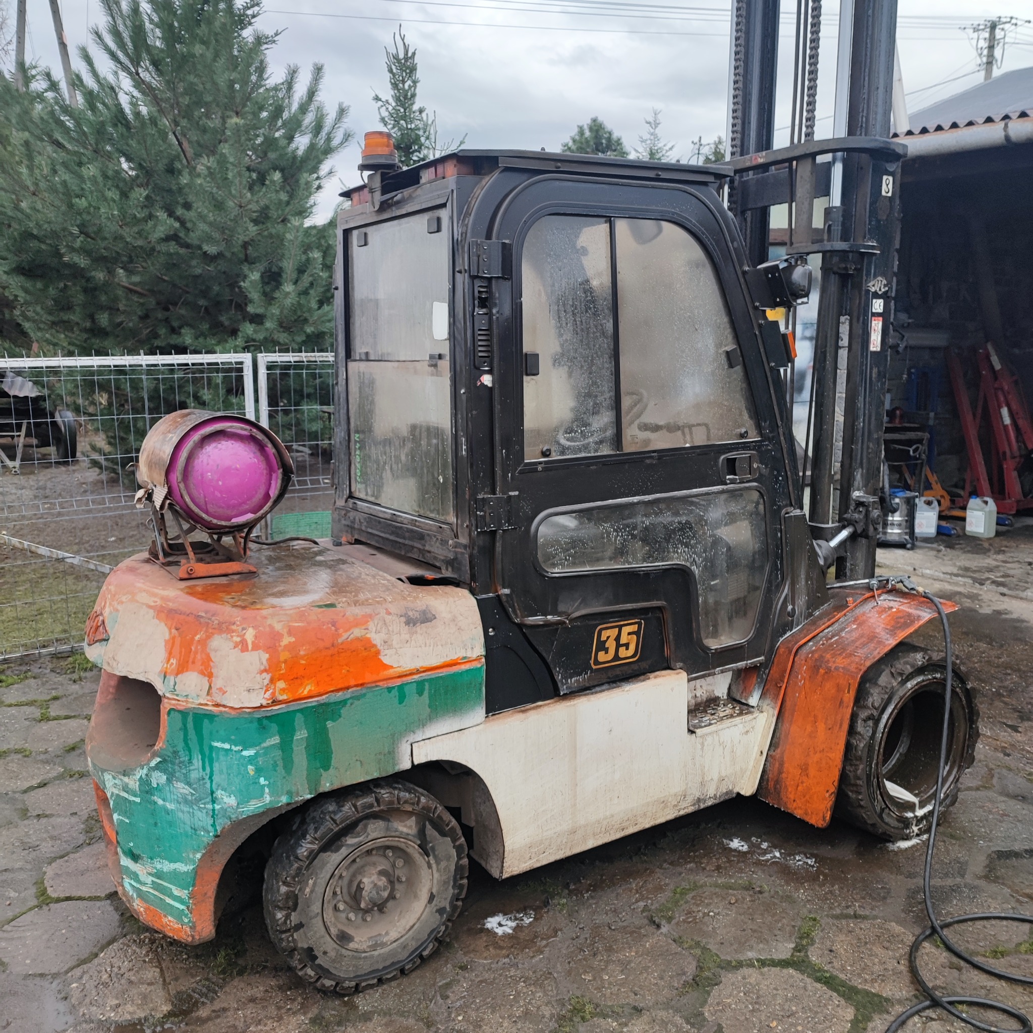 Wózek widłowy z numerem 35, z widocznymi śladami użytkowania, na zewnątrz. Charakterystyczny element: lampa ostrzegawcza z fioletowym szkłem.