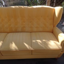 Czyste Meble Alex - Żółta kanapa z tapicerowanymi guzikami, widoczne plamy na siedzisku, sugerujące pranie. Ujęcie z bliska, na zewnątrz, w tle roślinność.