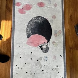 Czyste Meble Alex - Wzór dywanu z grafiką: leżąca postać kobiety na tle księżyca, wiszące abstrakcyjne lampy i trójkąty. Jasne tło, szara obwódka z frędzlami. Widoczne ślady po czyszczeniu.