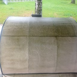 Czyste Meble Alex - Widok z bliska na czyszczoną, beżową kanapę ogrodową z widoczną różnicą w czystości po lewej stronie. Tło stanowi trawnik i drzewa.