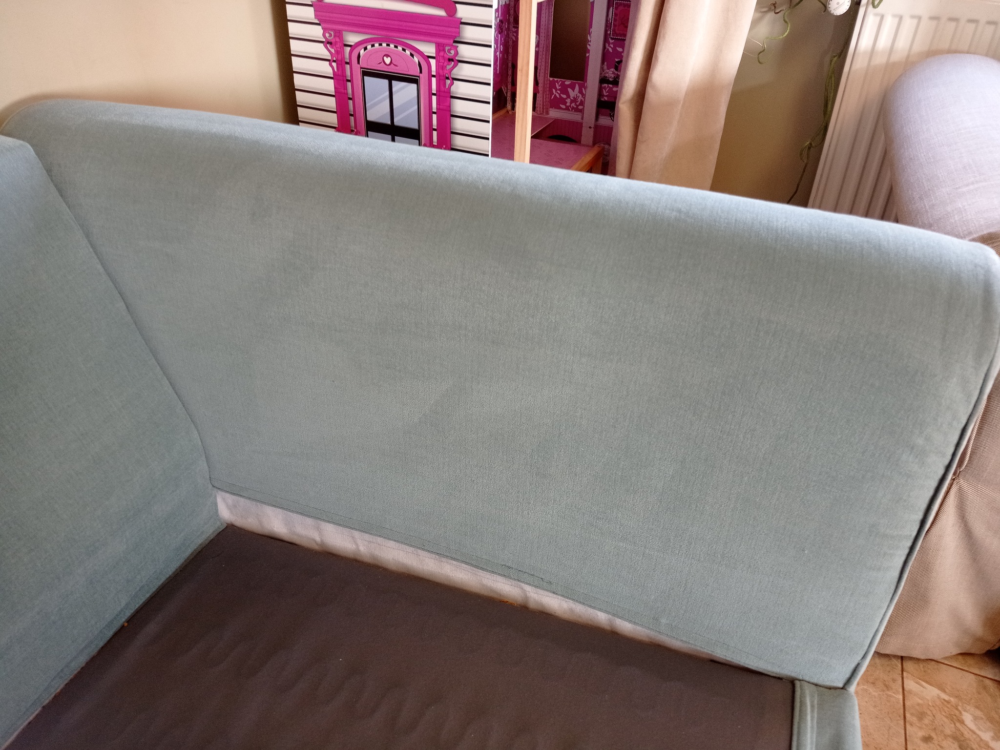 Jasnoniebieska kanapa z ciemnobrązowym siedziskiem, widoczna z bliska, z elementami dekoracyjnymi w tle, w tym domek dla lalek.