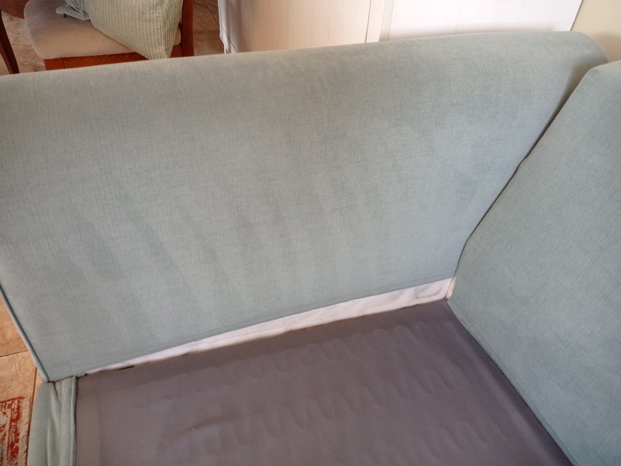 Jasnoniebieska kanapa z szarym siedziskiem, widok z góry pod kątem. Minimalistyczny design, gładka tapicerka, brak dekoracji.