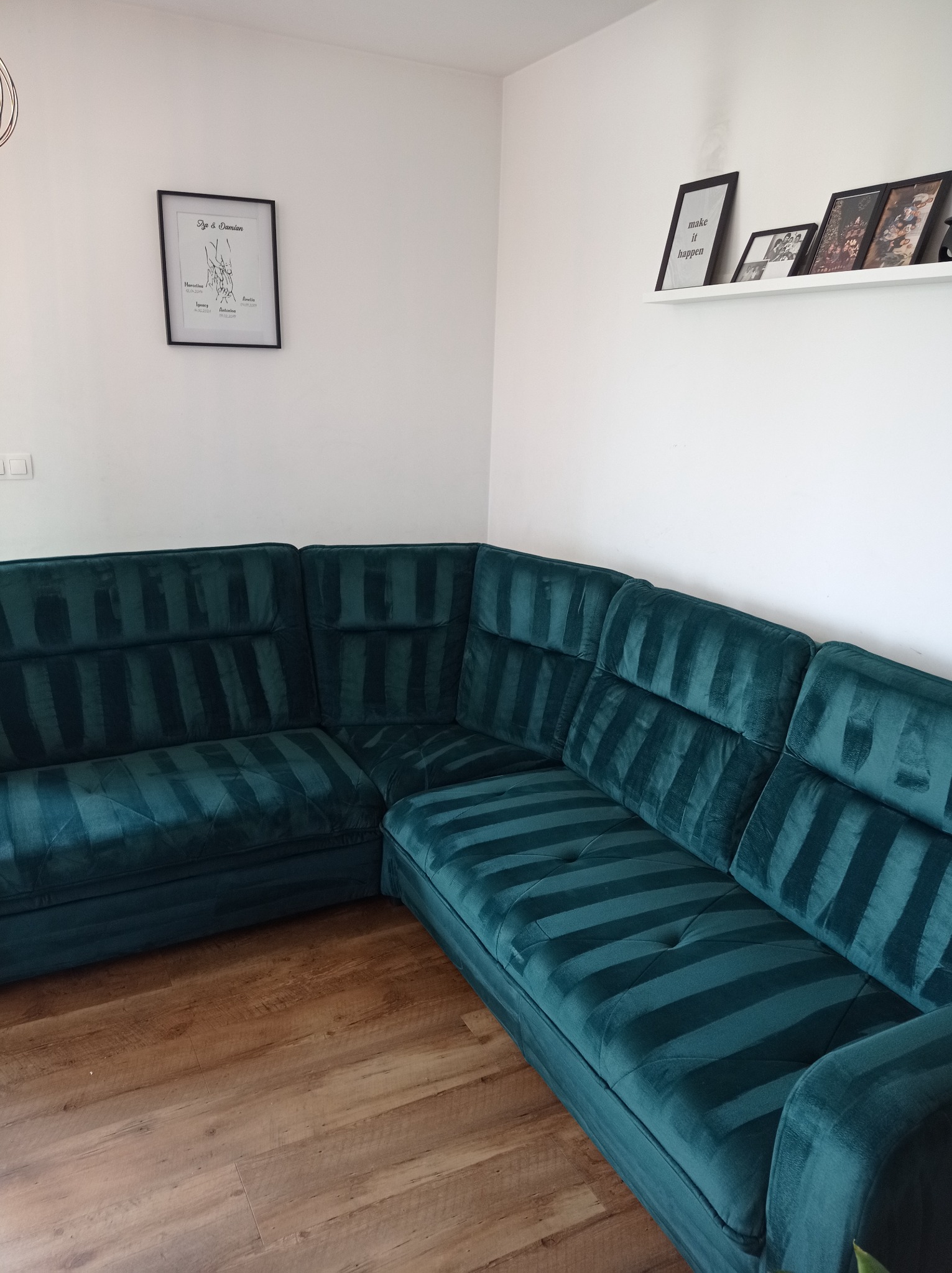 Szmaragdowy narożnik z aksamitną tapicerką w paski, drewniana podłoga, minimalistyczny wystrój wnętrza z ramkami na ścianie.