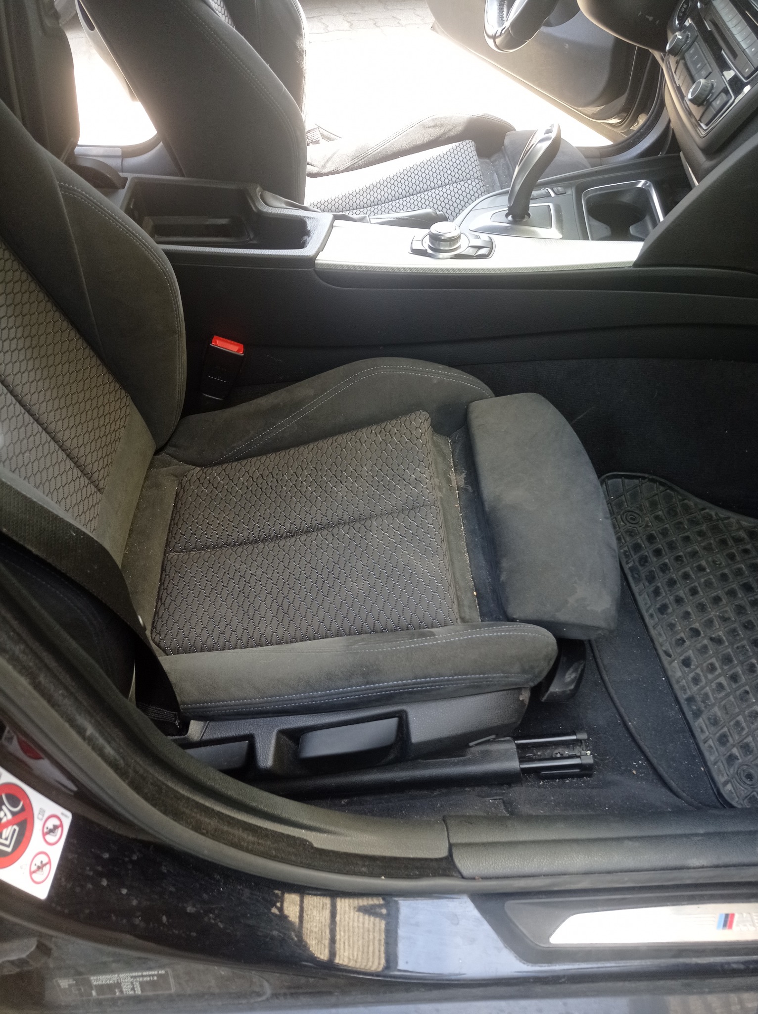 Brudna, szara tapicerka fotela samochodowego z widocznymi plamami i zabrudzeniami, wnętrze pojazdu z elementami deski rozdzielczej i podłogi.