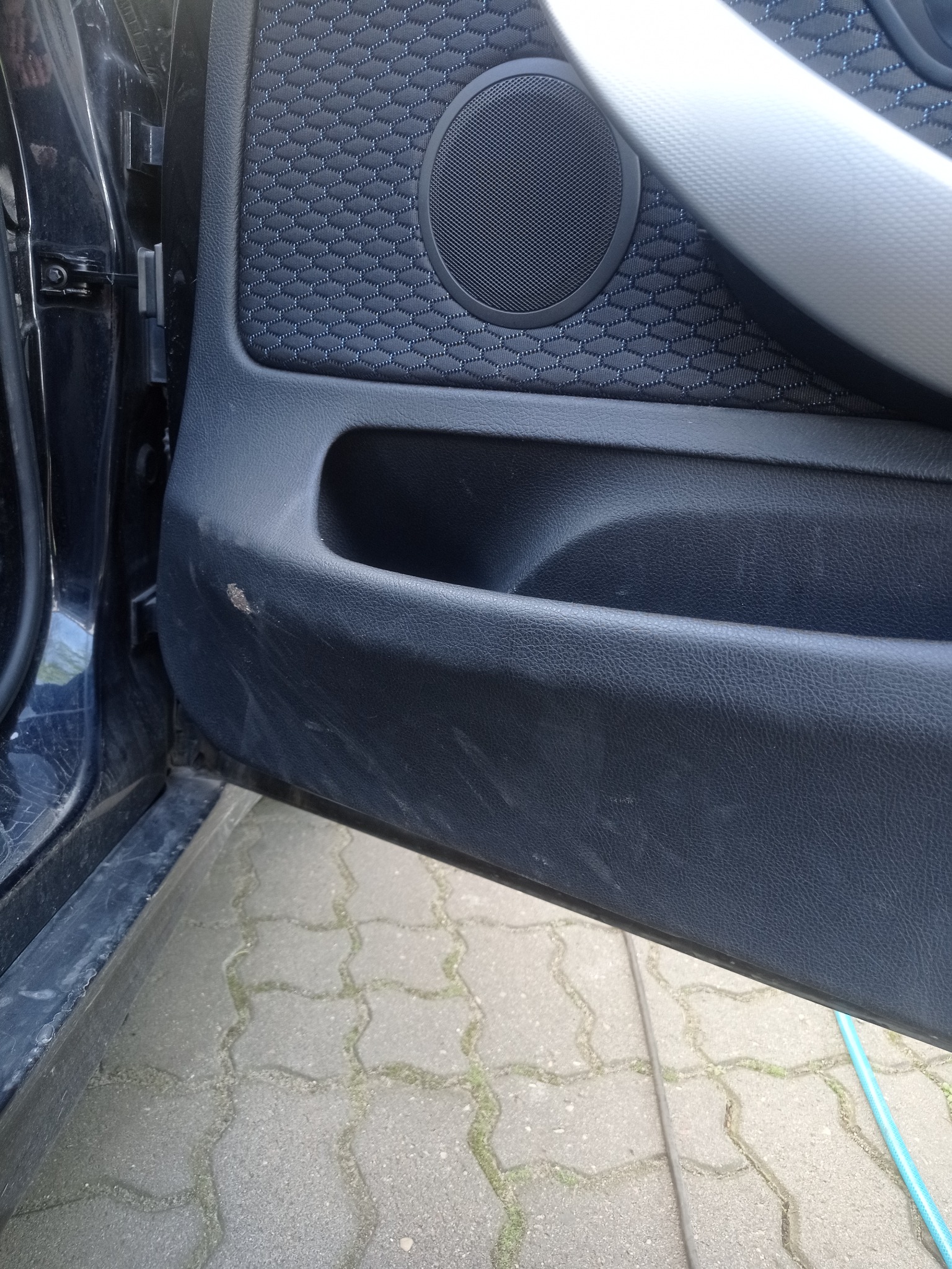 Brudny panel drzwi samochodu z widocznymi plamami i zabrudzeniami, ukazujący potrzebę czyszczenia tapicerki samochodowej. Teksturowana powierzchnia, widoczny głośnik.