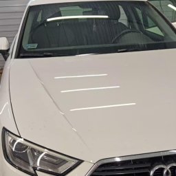 takieczyste.pl Rafał Sujecki - Białe Audi A3 w warsztacie z widoczną tablicą rejestracyjną, ukazujące detale karoserii i reflektorów, sugerujące mycie lub detailing.