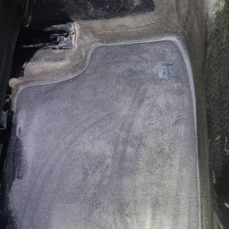 takieczyste.pl Rafał Sujecki - Wnętrze samochodu po czyszczeniu: jasna piana na dywanikach i podłodze, detale konsoli środkowej. Widoczne ślady detergentu, sugerujące świeżo wykonaną usługę.