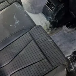 Wnętrze samochodu po czyszczeniu: widoczne mokre fotele z tkaniny w prążki i wilgotna podłoga, pozostałości po praniu. Detal na kratce wentylacyjnej.