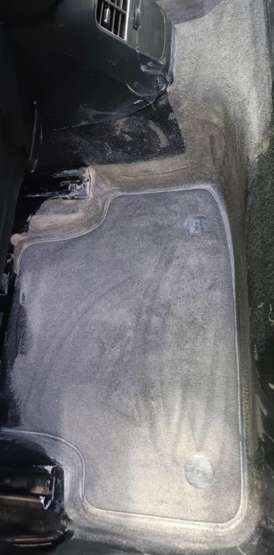 Wnętrze samochodu po czyszczeniu: jasna piana na dywanikach i podłodze, detale konsoli środkowej. Widoczne ślady detergentu, sugerujące świeżo wykonaną usługę.