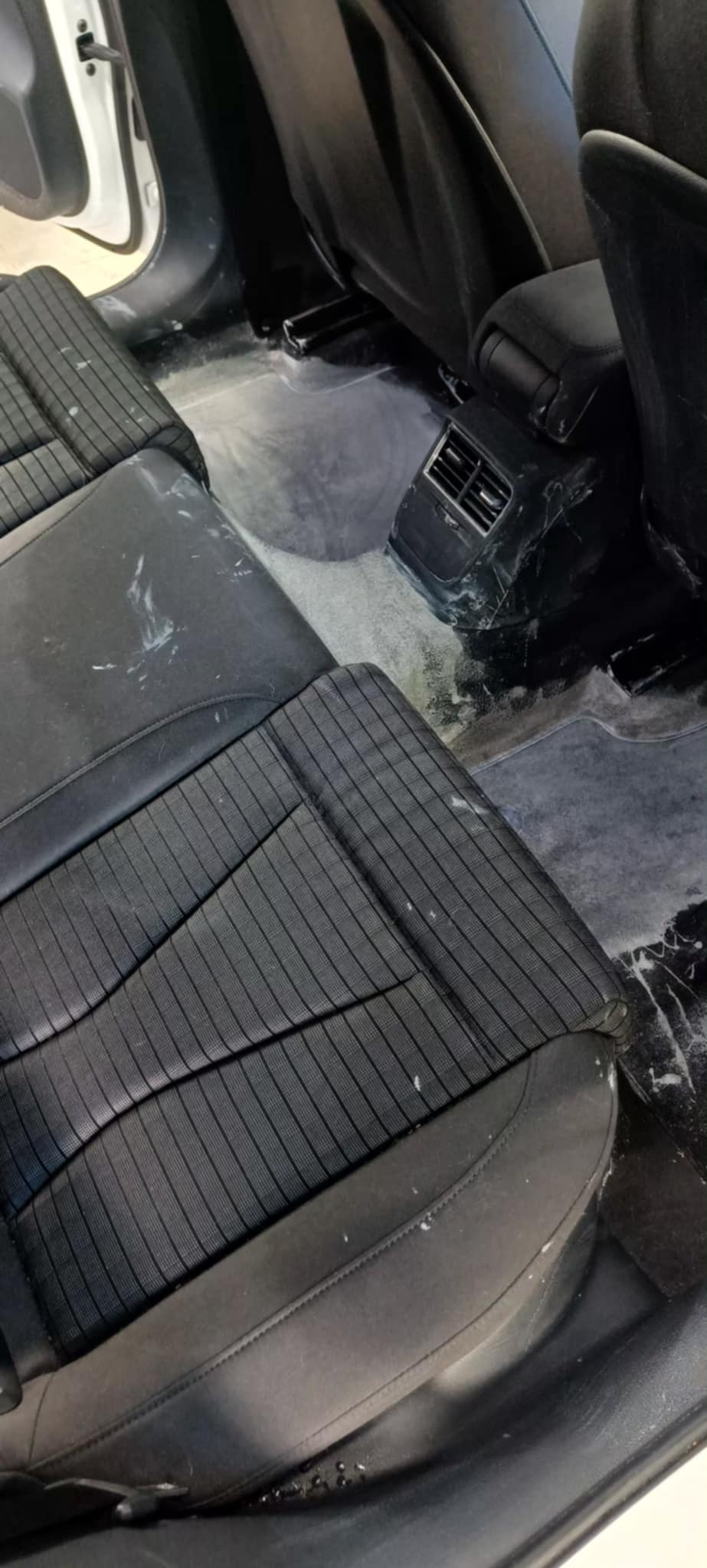 Wnętrze samochodu po czyszczeniu: widoczne mokre fotele z tkaniny w prążki i wilgotna podłoga, pozostałości po praniu. Detal na kratce wentylacyjnej.