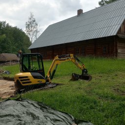 Kopman Robert Palewicz - Żółta mini koparka Yanmar SV26 na trawiastym terenie, z drewnianym budynkiem w tle, obok wykopany rów, przykryty częściowo zieloną plandeką.