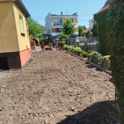 RAM-BUD - Przygotowany teren pod budowę z widocznym minikoparką CAT i częściowo wykończonym obrzeżem. Słoneczny dzień, widok na domy w tle.