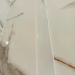 Detal wykończenia: narożnik z białych, marmurkowych płytek. Widoczne fugi i precyzja ułożenia. Nowoczesny design łazienki z bliska.